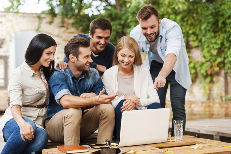 It is brilliant idea! Group of joyful young people looking at laptop while working together outdoors
